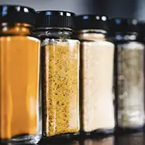 Four glass jars with black lids containing dry pantry staples and spices