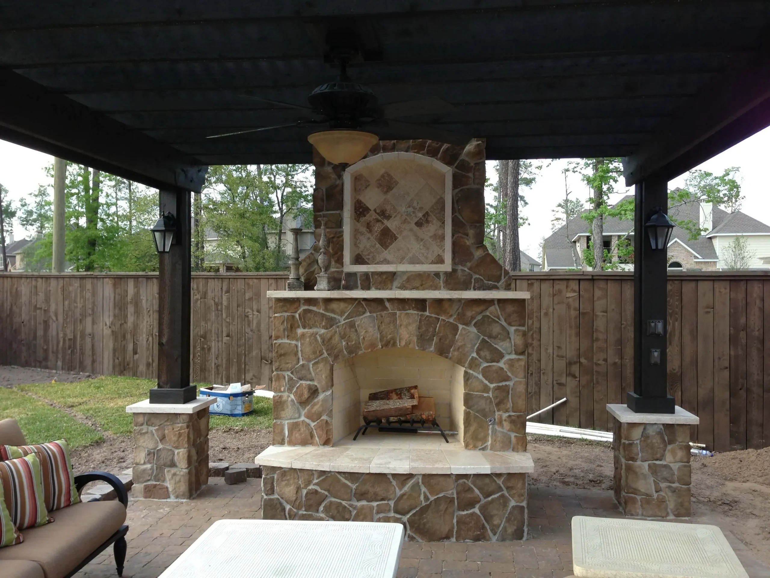 Luxury outdoor fireplace with stone construction under covered patio in Woodlands backyard entertainment space