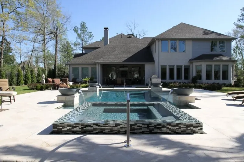 Luxury backyard pool with geometric design, glass tile spa, and water features adjacent to modern home