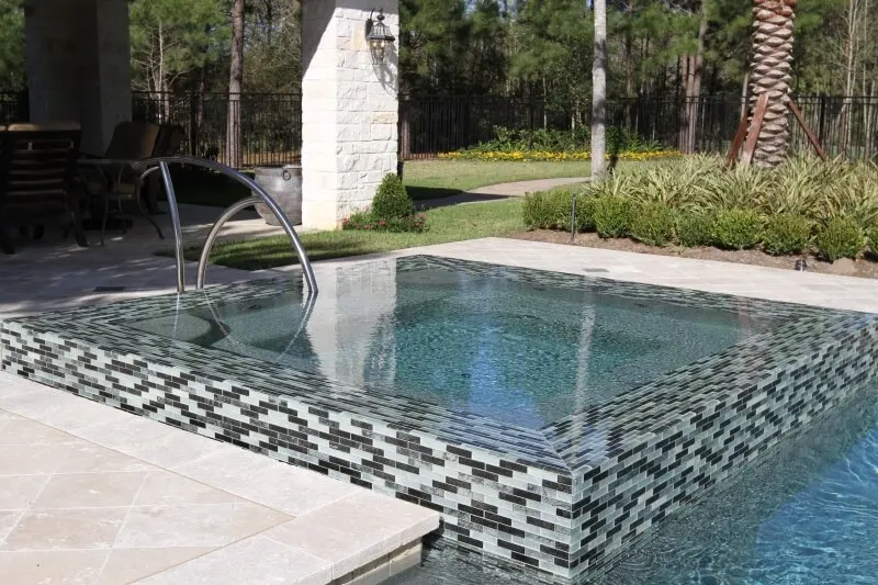 Modern luxury backyard pool with glass tile spa and sleek metal handrail design