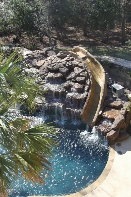 Luxury backyard pool with natural rock waterfall and water slide featuring turquoise water and tropical landscaping