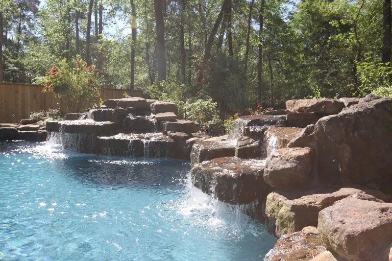 Luxury natural stone pool with cascading waterfall surrounded by forest trees and woodland landscape