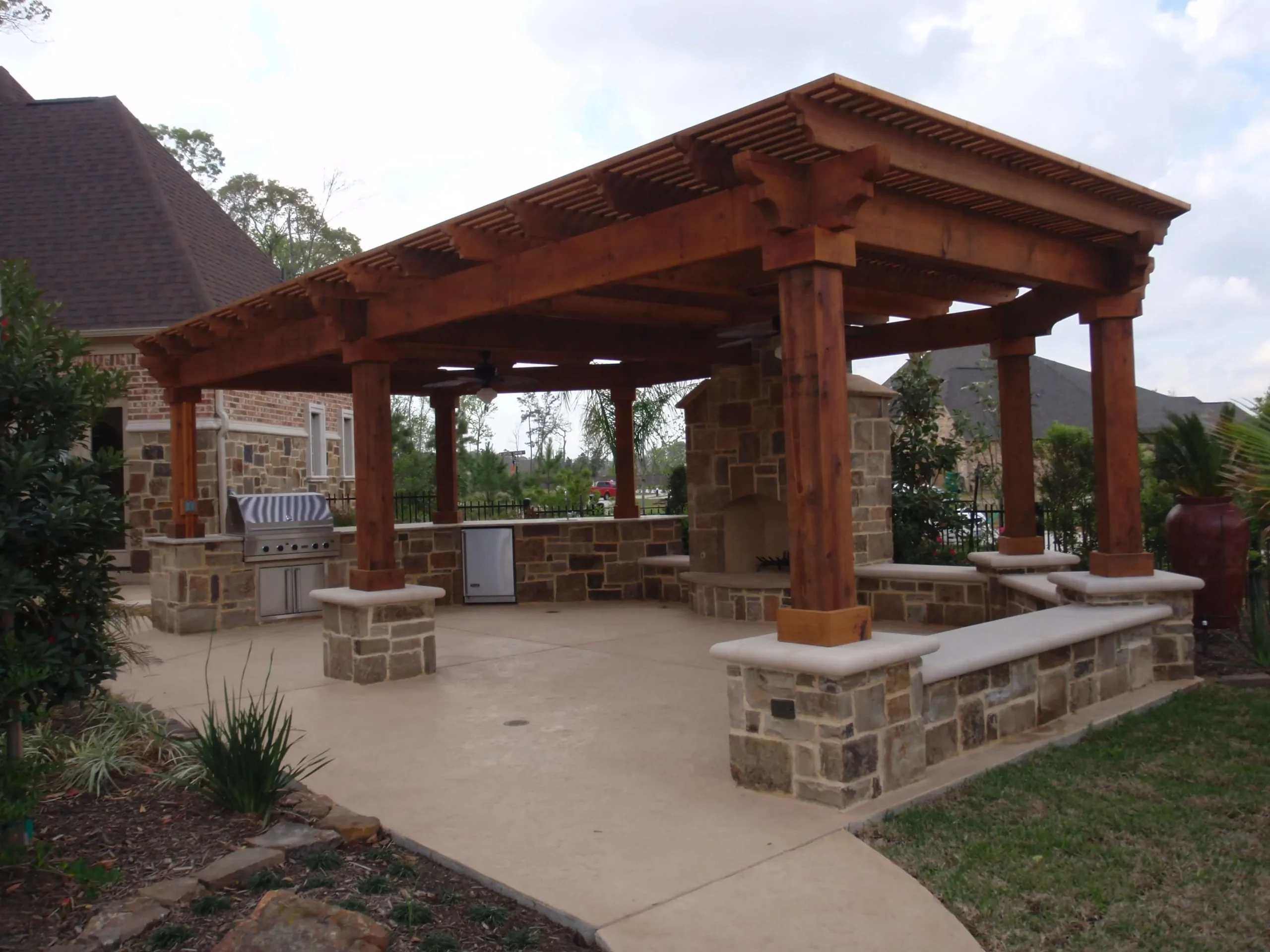 Luxury outdoor kitchen and pergola with stone fireplace and seating in Woodlands backyard entertainment space