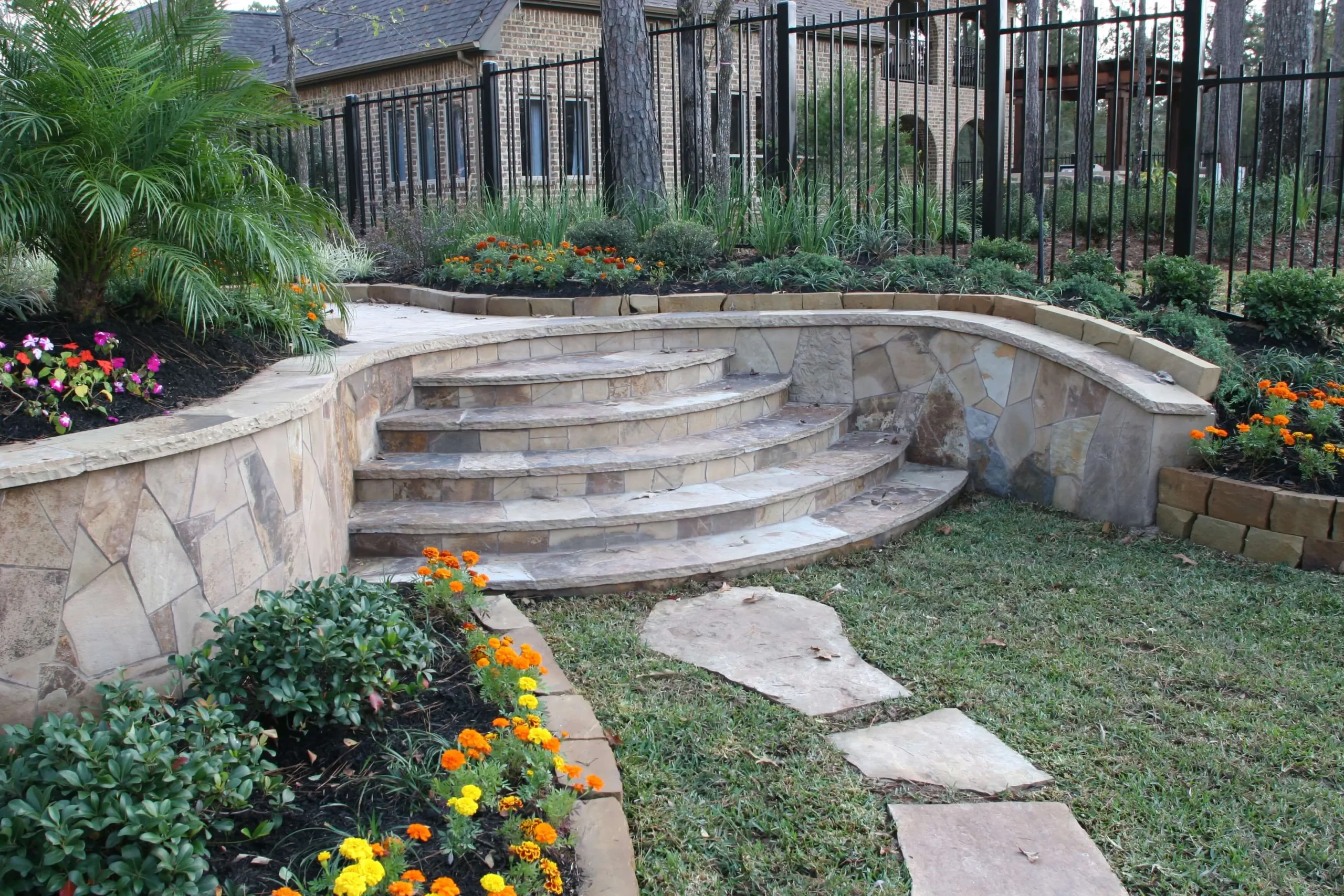 Curved stone patio steps with raised garden beds and black metal fencing in luxury backyard outdoor living space