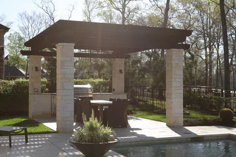 Modern stone pergola with integrated outdoor kitchen and grill in luxury backyard entertainment space