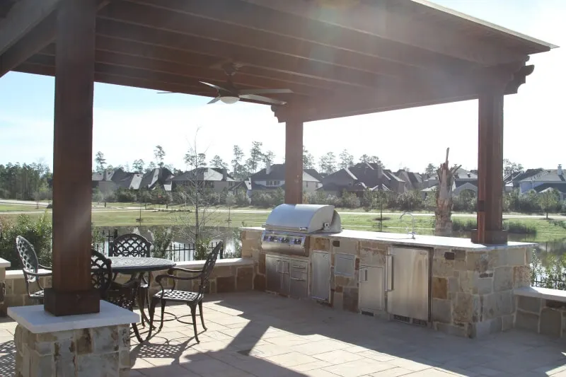 Luxury backyard entertainment space with pergola, outdoor kitchen, and poolside patio overlooking water