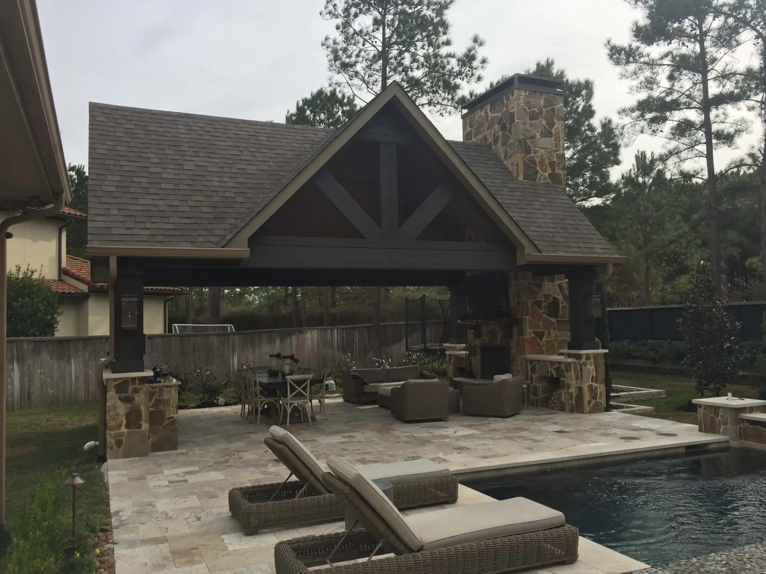 Luxury backyard with custom swimming pool, stone patio, fireplace chimney, and covered outdoor entertainment pavilion