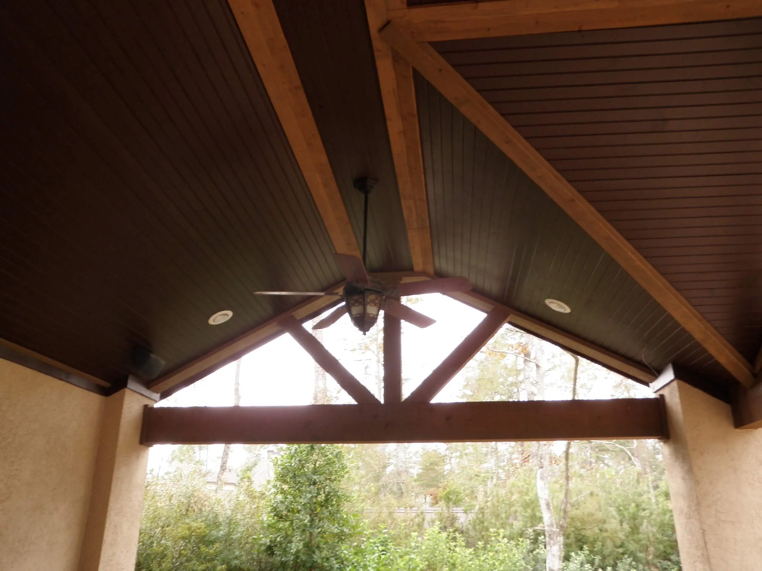 Modern wooden pergola with ceiling fan overlooking lush backyard trees and outdoor living space