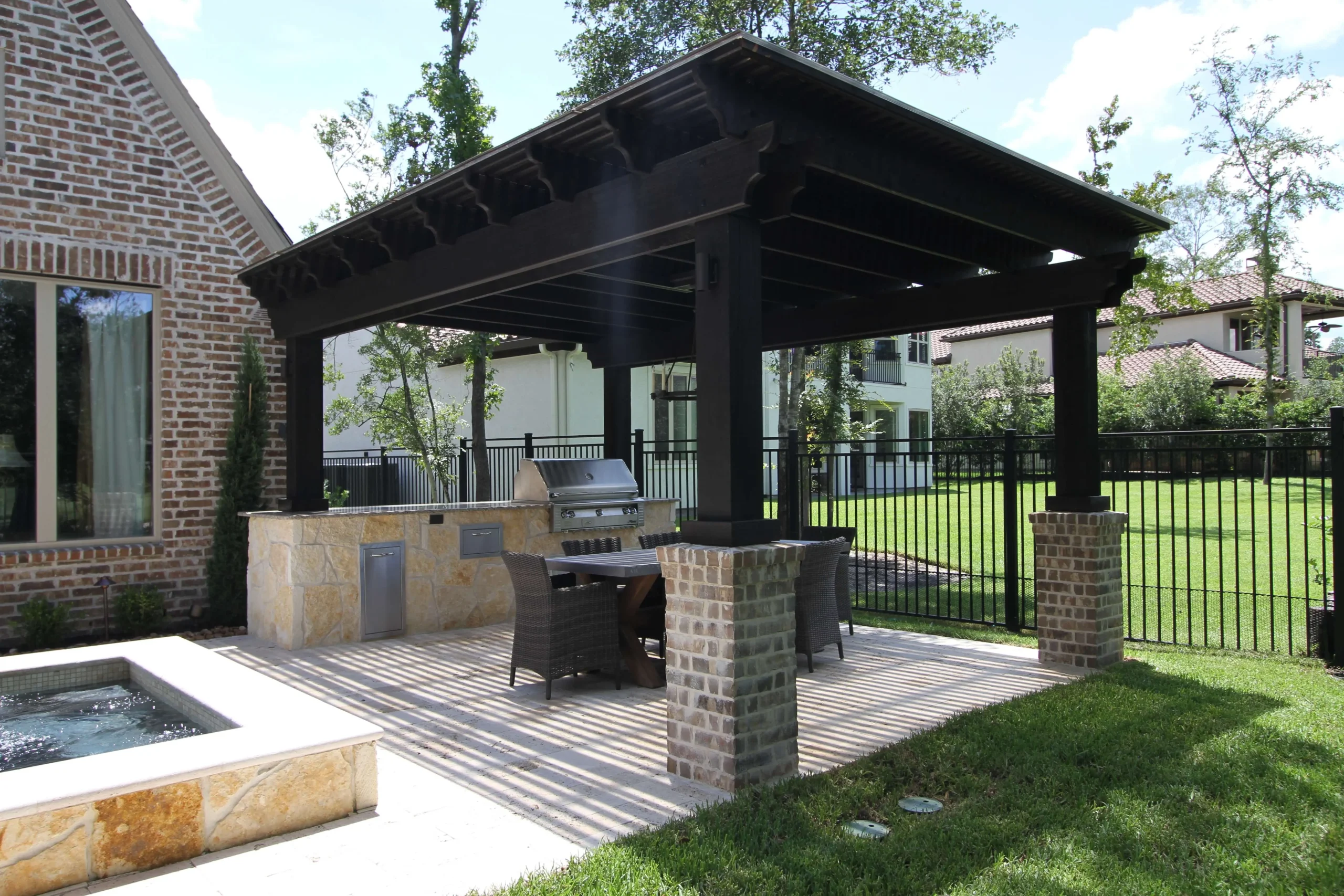 Black pergola with integrated outdoor kitchen and dining area overlooking luxury backyard pool