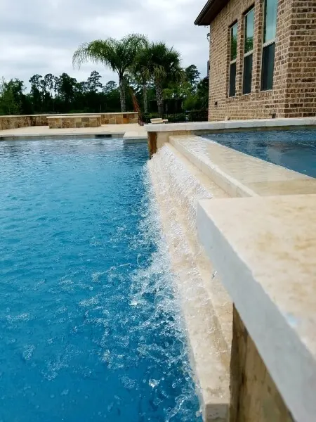 Luxury custom pool with elegant stone coping and water feature overlooking tropical backyard