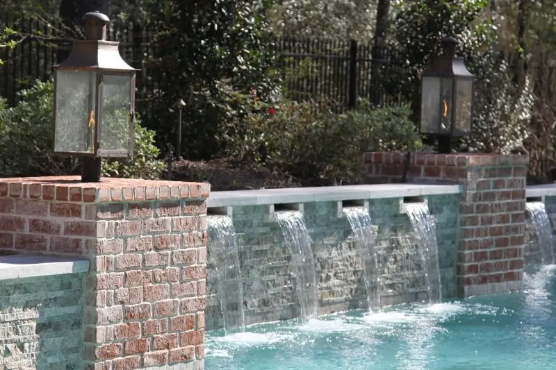 Luxury backyard pool with cascading sheer descent water features and decorative gas lanterns