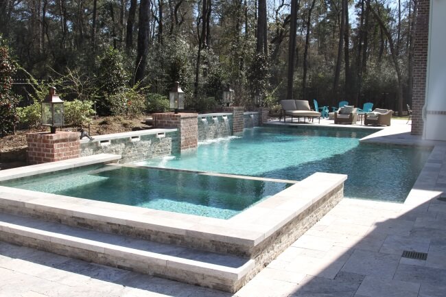 Luxury backyard pool and spa with custom stone patio and outdoor entertainment area surrounded by trees