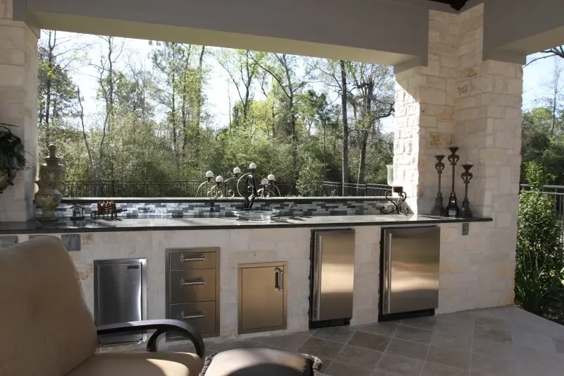 Luxury outdoor kitchen with stainless steel appliances and custom pool design in Woodlands backyard entertainment space